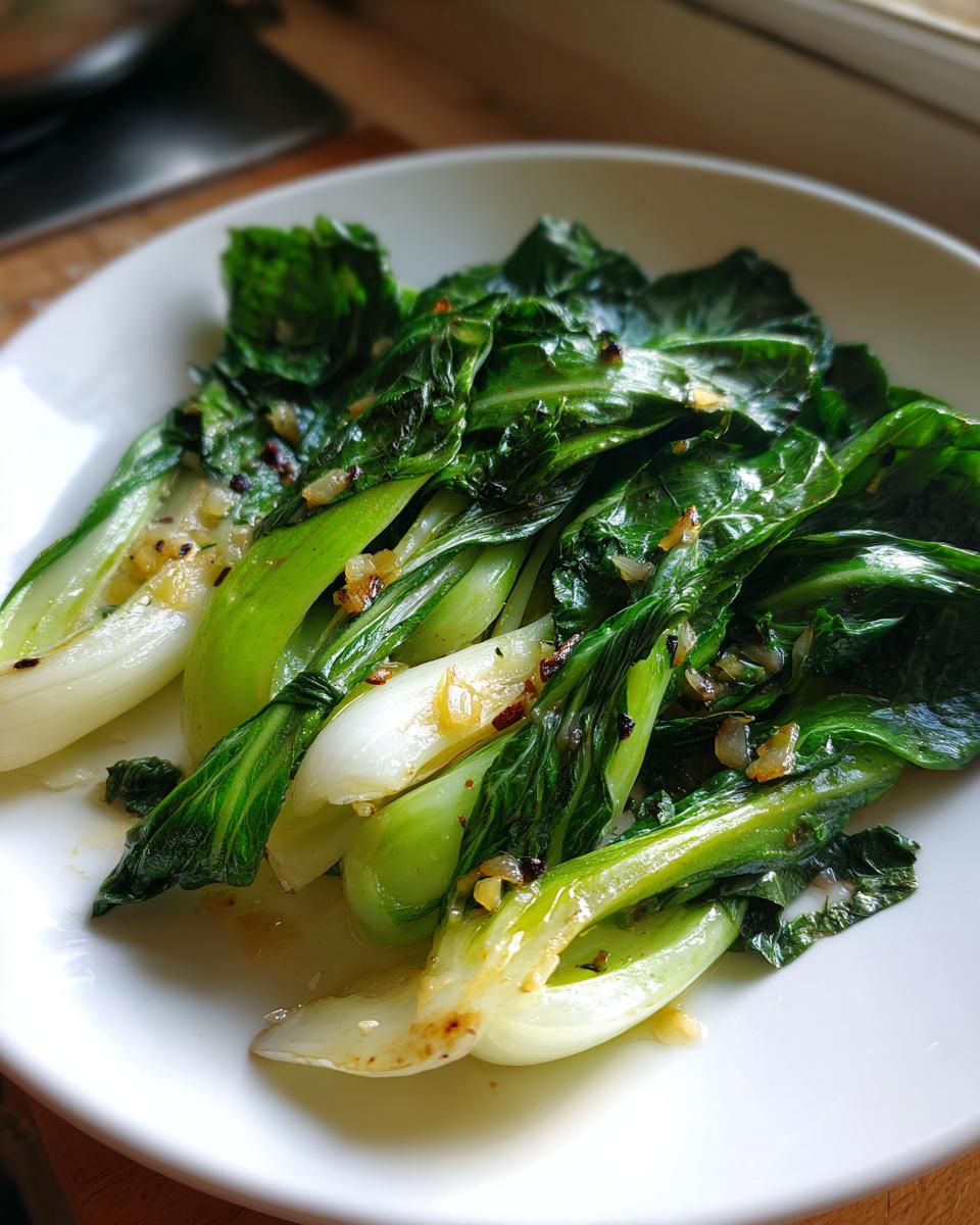 Close-up of vibrant green Sautéed bok choy with garlic served on a white plate.