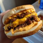 A person holding a juicy double patty smash burger recipe with special sauce, melted cheese dripping down the sides.