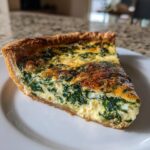 Close-up of a perfectly baked slice of spinach and cheese quiche on a white plate.