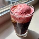 Close-up of a cold glass of iced coffee topped with vibrant pink strawberry cold foam coffee.