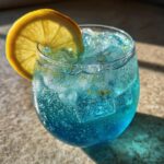 Close-up of a vibrant blue, bubbly Refreshing Moscato spritz cocktail filled with ice and garnished with a bright lemon slice.