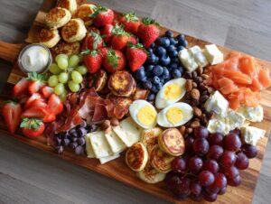 A vibrant overhead view of a large Breakfast grazing board featuring mini pancakes, strawberries, blueberries, grapes, smoked salmon, and cheese.